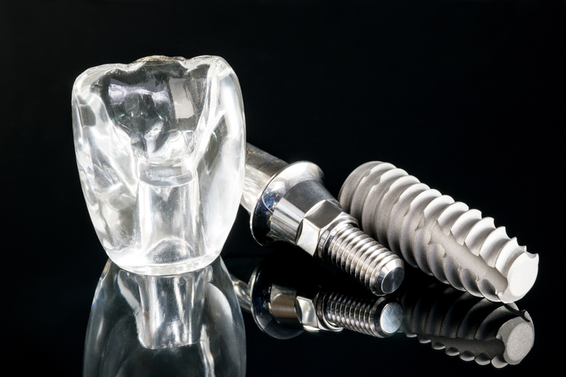 Close-up dental implant model on a black glass table and background.